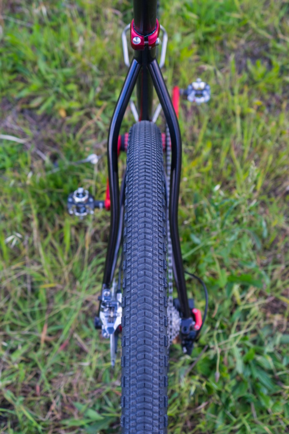 Black seat stays and gravel tire seen from behind, with a red seat clamp