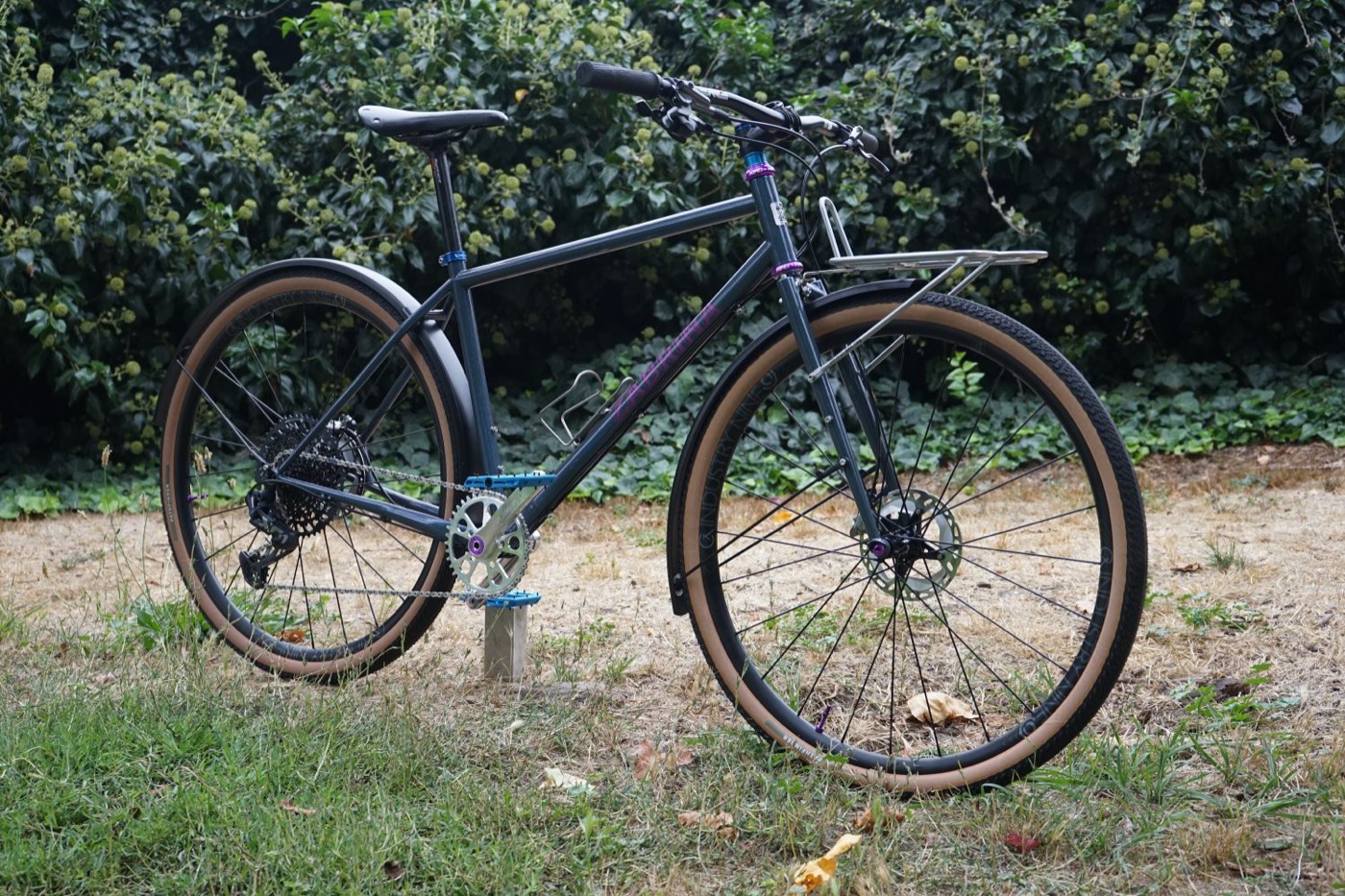 Slate blue flat-bar gravel bike with front rack, fenders and purple accents