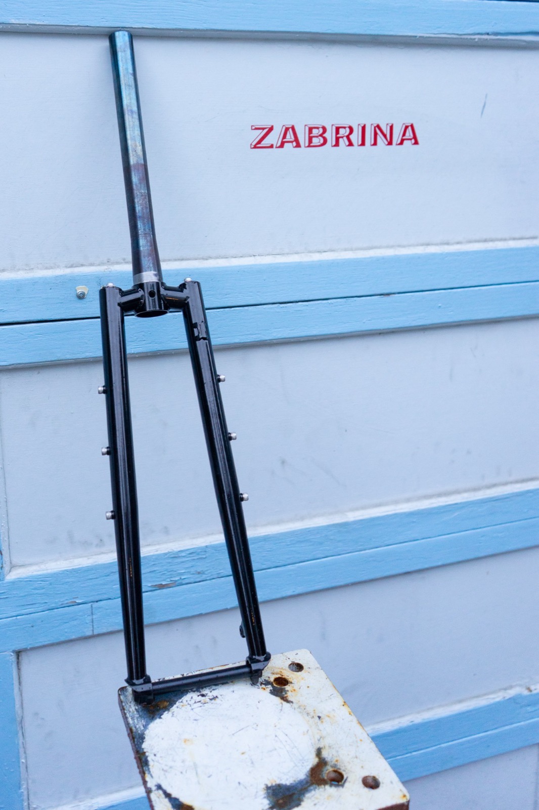 Black segmented steel fork leaning on a light blue and white garage door painted with ZABRINA