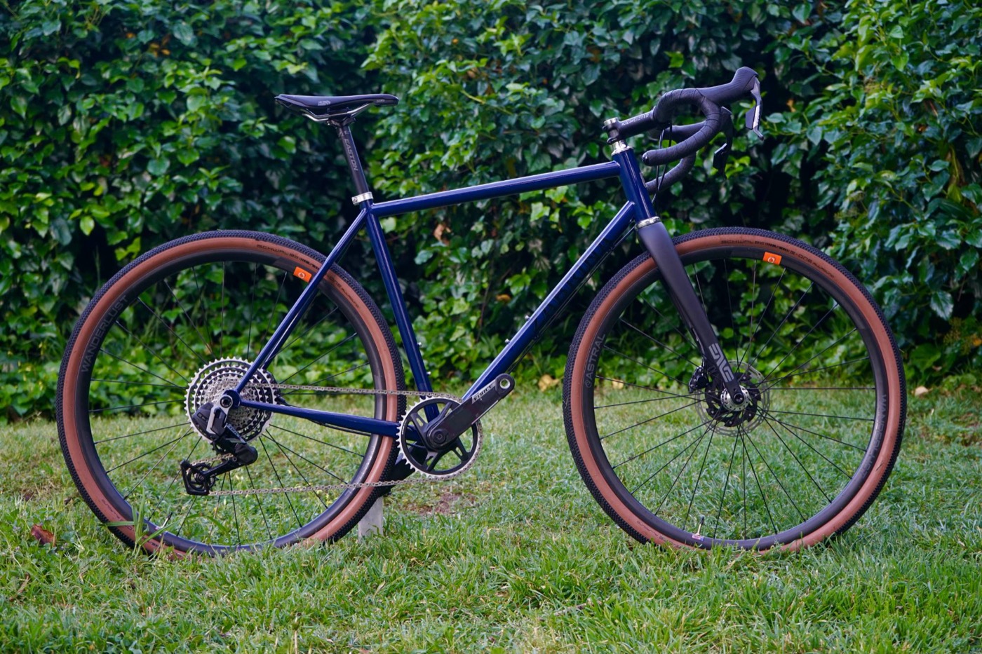 Navy drop-bar gravel bike with tan-wall tires on grass in front of ivy