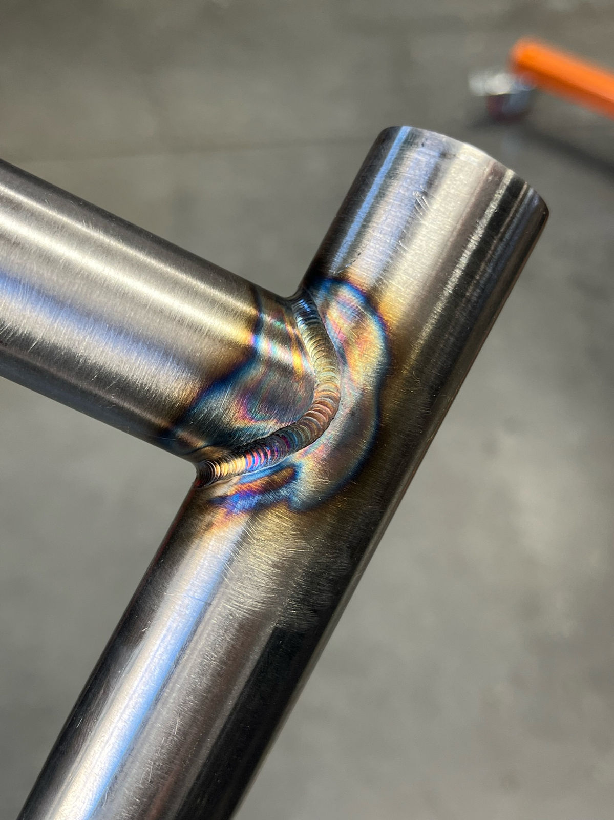 TIG weld glowing with heat tint where two polished steel tubes meet