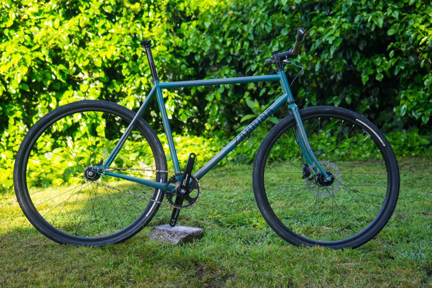 Teal single-speed Zabrina with a sparkle finish on grass in front of bright green leaves
